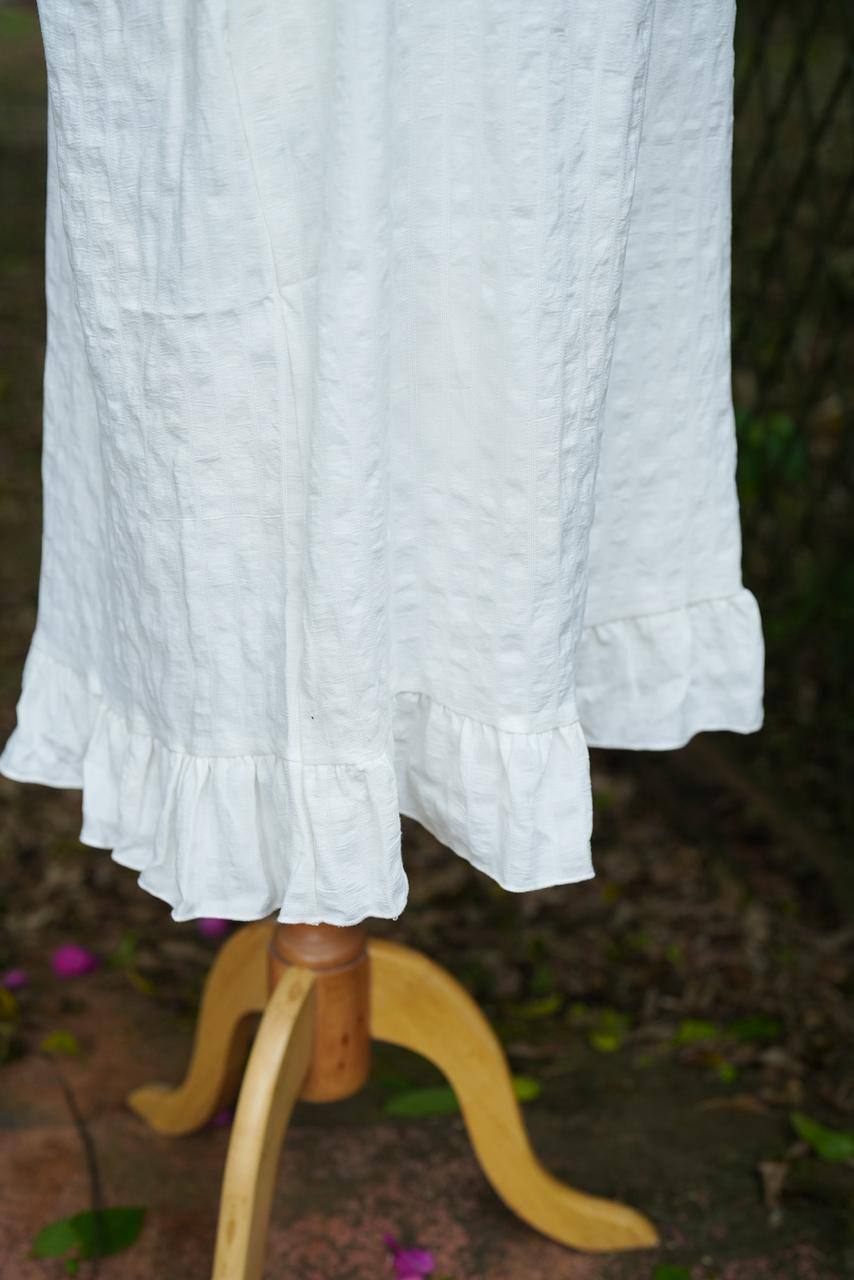 White dress with ruffled hem on a wooden stand against a natural background