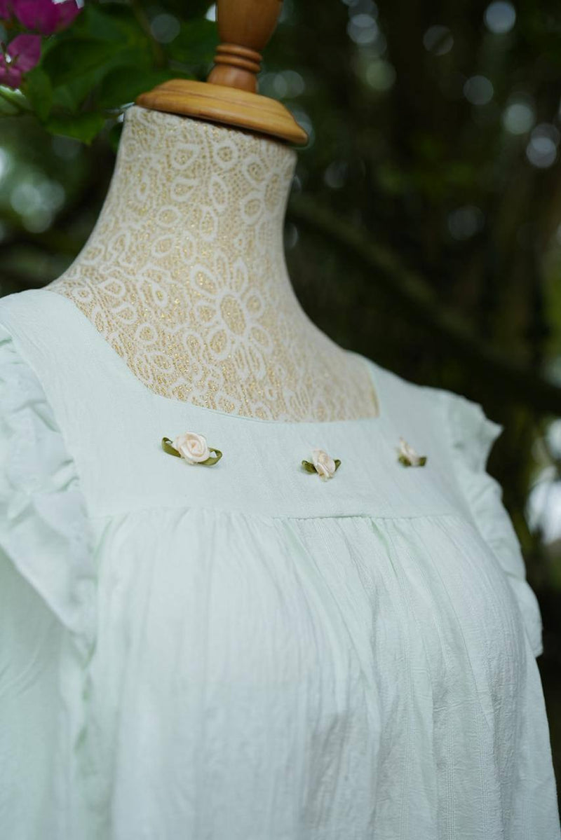 White lace dress on a mannequin with floral embroidery against a blurred natural background